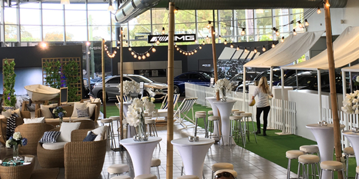 Car dealership lounge area featuring multiple seating arrangements with woven furniture, small tables, and artificial grass flooring.