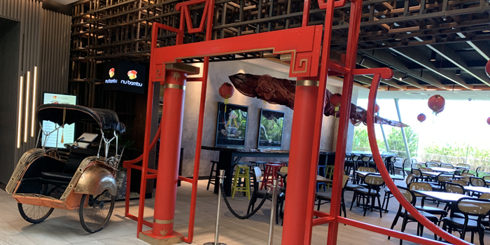 Ornate rickshaw on display in an indoor space with red decorative arch and seating area. Restaurant setting with ambient lighting.