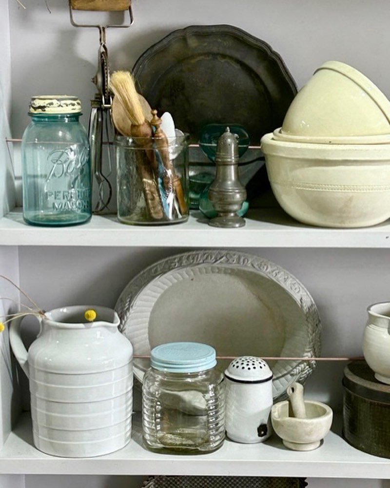 Still life of vintage kitchenware, featuring jars, bowls, and utensils arranged on shelves, creating a rustic aesthetic.
