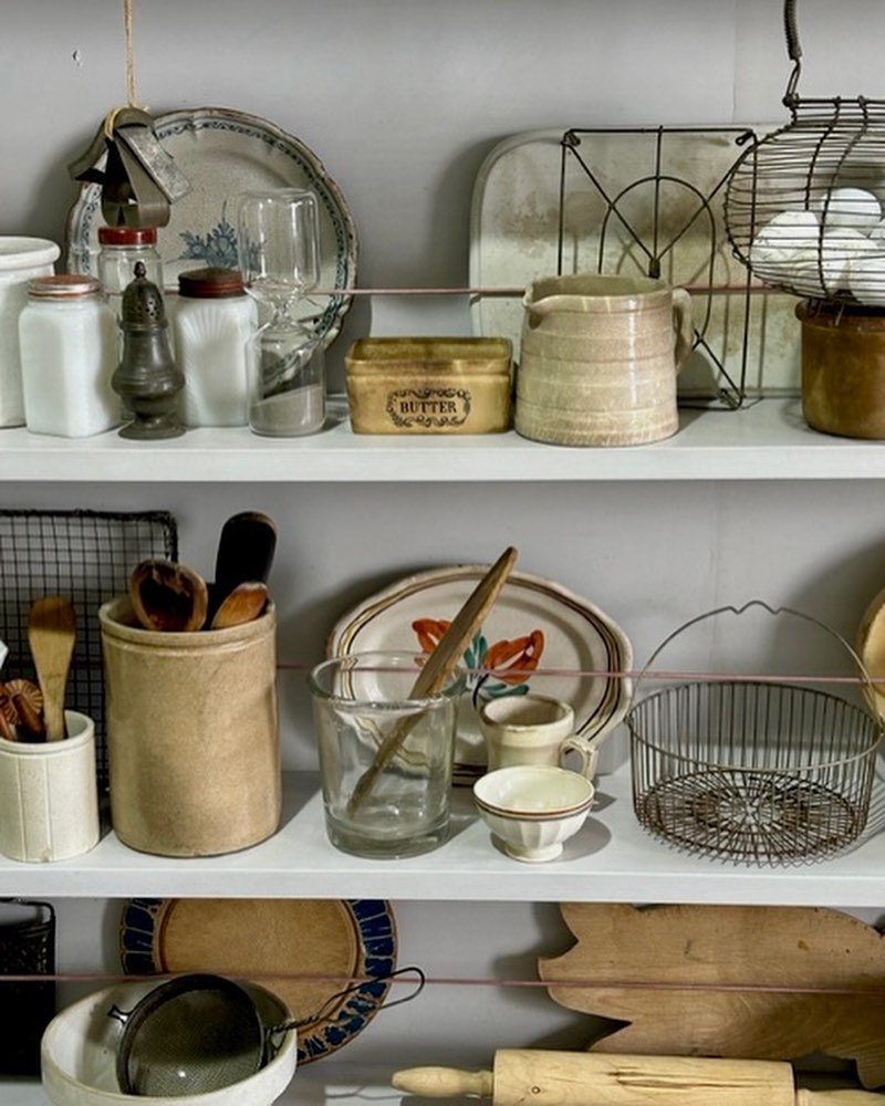 Still life featuring an arrangement of vintage kitchenware and dishware displayed on white shelves against a grey wall backdrop.