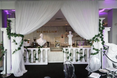 Event bar setup featuring classical white pillars, draped white fabric, and decorative ivy styled by Sydney Props.