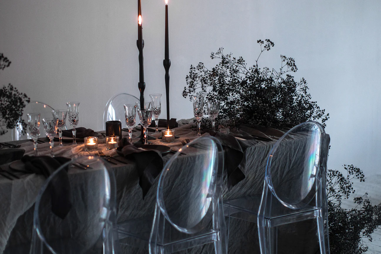 Table setting with black candles and transparent chairs, illuminated by candlelight against a neutral background, evoking elegance.