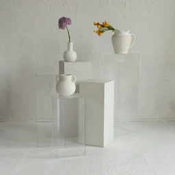 White ceramic vases and floral arrangements on clear acrylic and white pedestals against a white brick wall in Sydney.