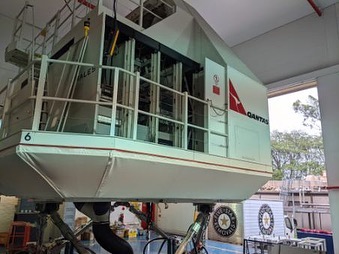 Flight simulator with Qantas logo in an indoor setting showing the equipment's intricate mechanical support system and interior components.