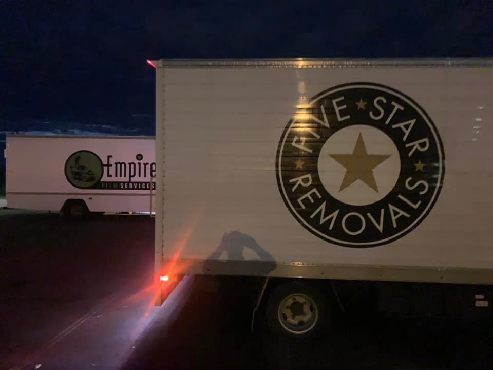 Two white box trucks parked at night. Truck on the right has the words 'Five Star Removals' written on the side of the truck.