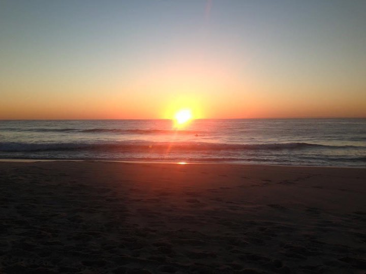 Golden sunset over the ocean, with calm waves gently lapping the sandy beach creating a tranquil, natural landscape.