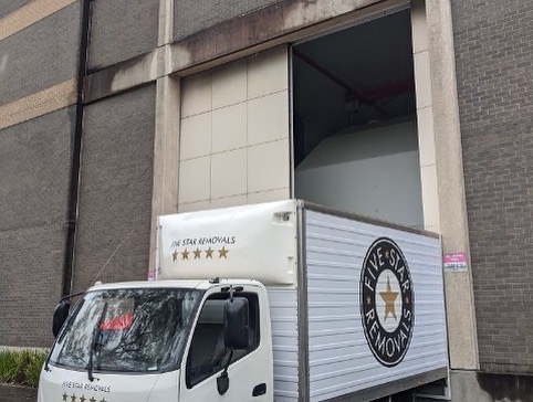 Moving truck parked outside a loading dock with 'Five Star Removals' logo; a commercial vehicle for transport and relocation services.