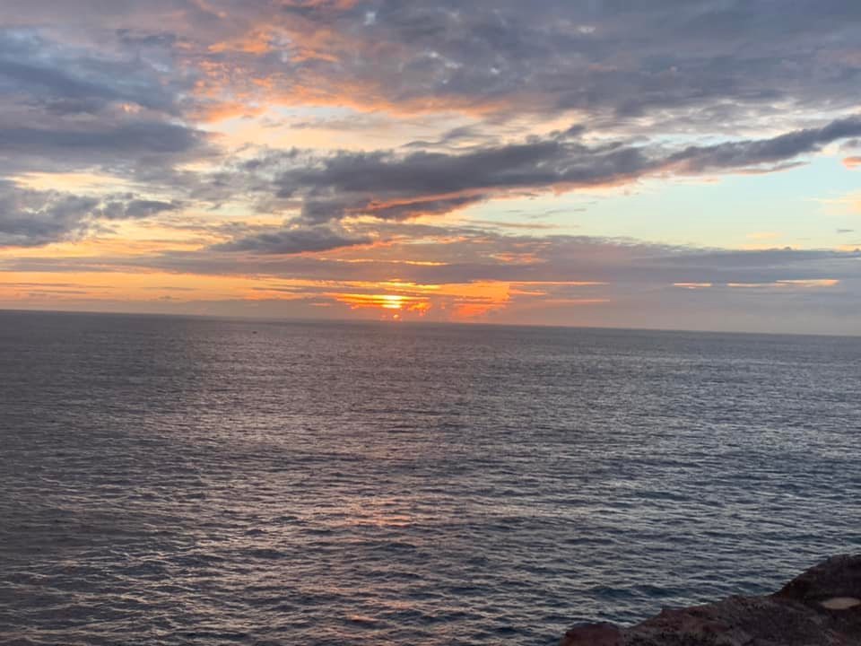 Scenic view of the ocean at sunset with colorful clouds and sun rays reflecting on the water's surface, creating a tranquil atmosphere.