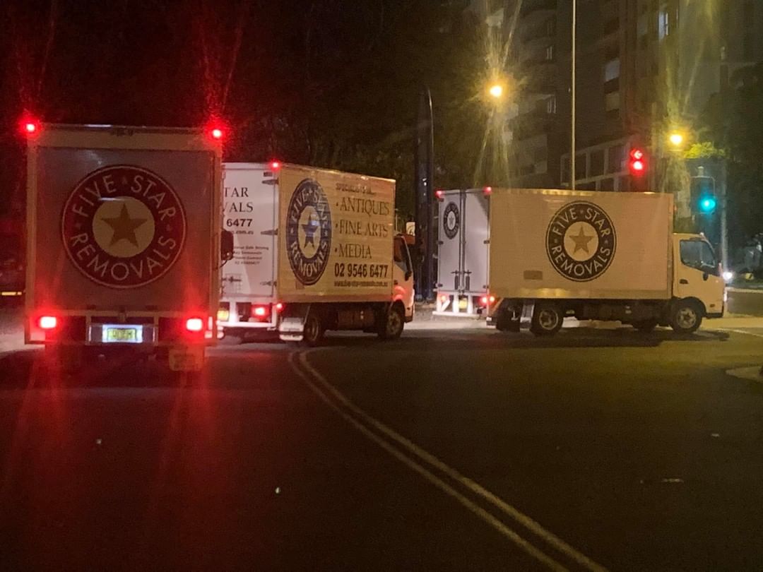 Five Star Removals trucks parked at night in city, street lights illuminate the scene with building in background, logistics theme.