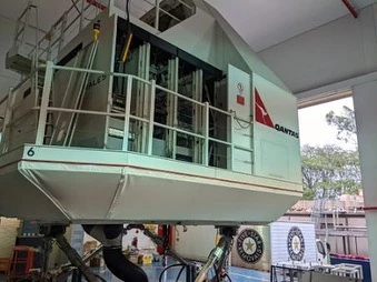 A white flight simulator cabin resting on hydraulic legs inside a large industrial facility in Sydney.
