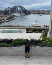 Man standing on a rooftop balcony overlooking Sydney Harbour and the Harbour Bridge