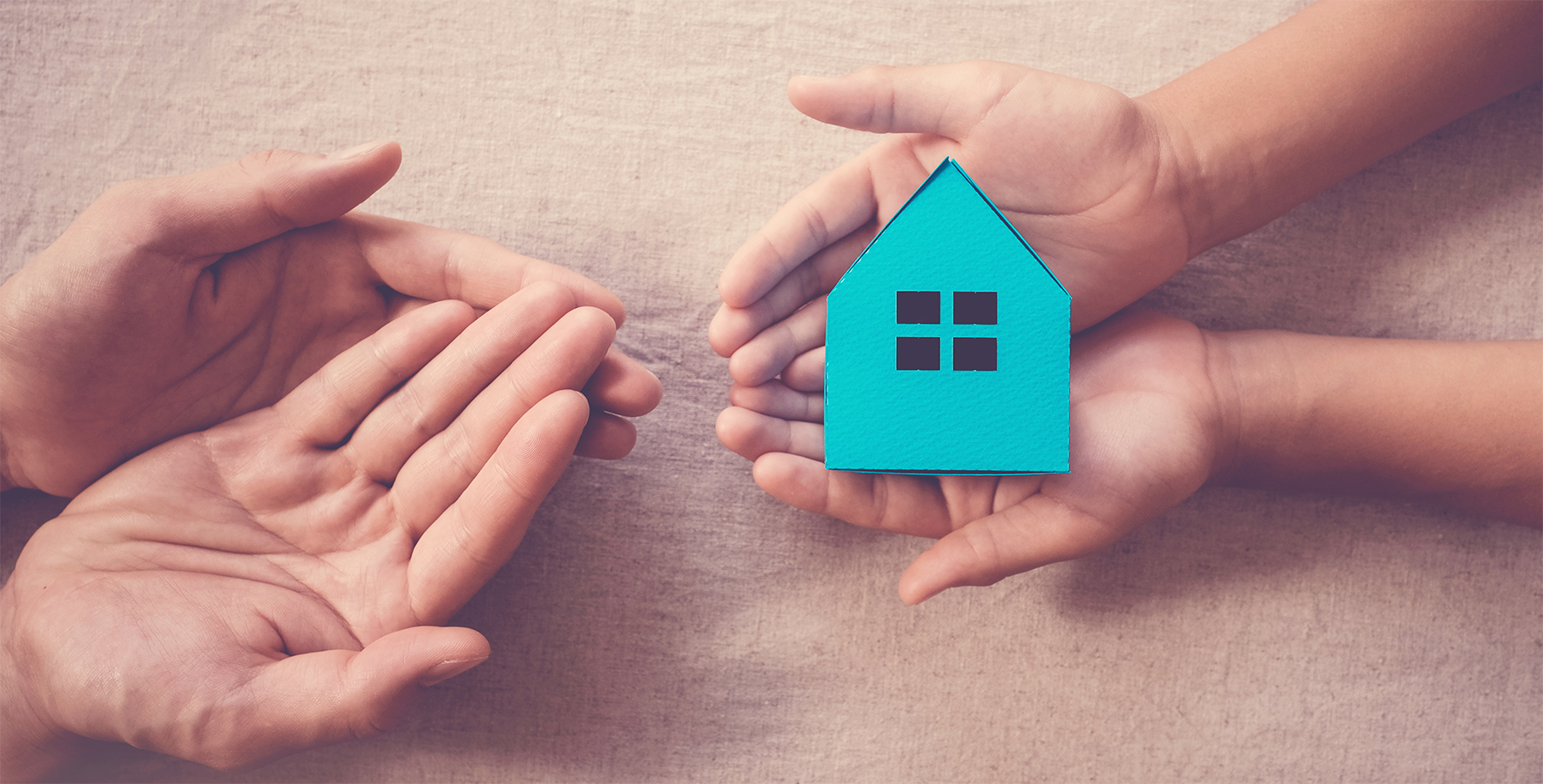 Hands holding a blue house, representing home ownership and family. Adult and child hands cradle the paper house on a textured background.