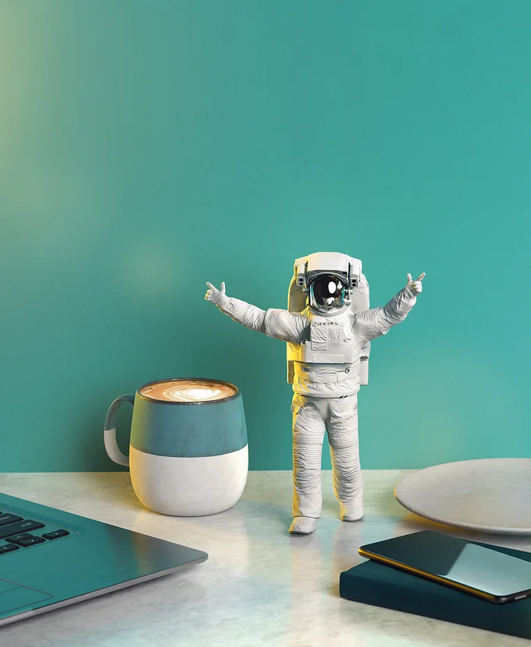 Astronaut figurine with raised arms on a desk, with a latte, laptop, plate, and phone, set against a teal background.