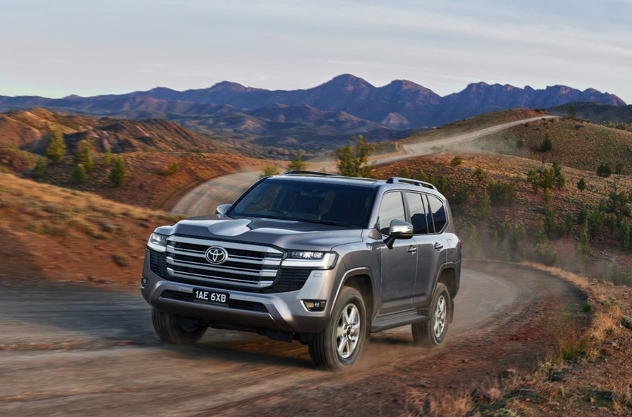 Gray Toyota Land Cruiser SUV driving on a dirt road in a mountainous landscape on a sunny day, showcasing its rugged design.