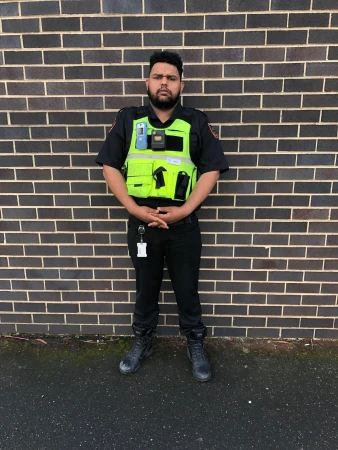 Standing portrait of adult male in a black uniform and neon yellow vest with a brick wall background on an overcast day.