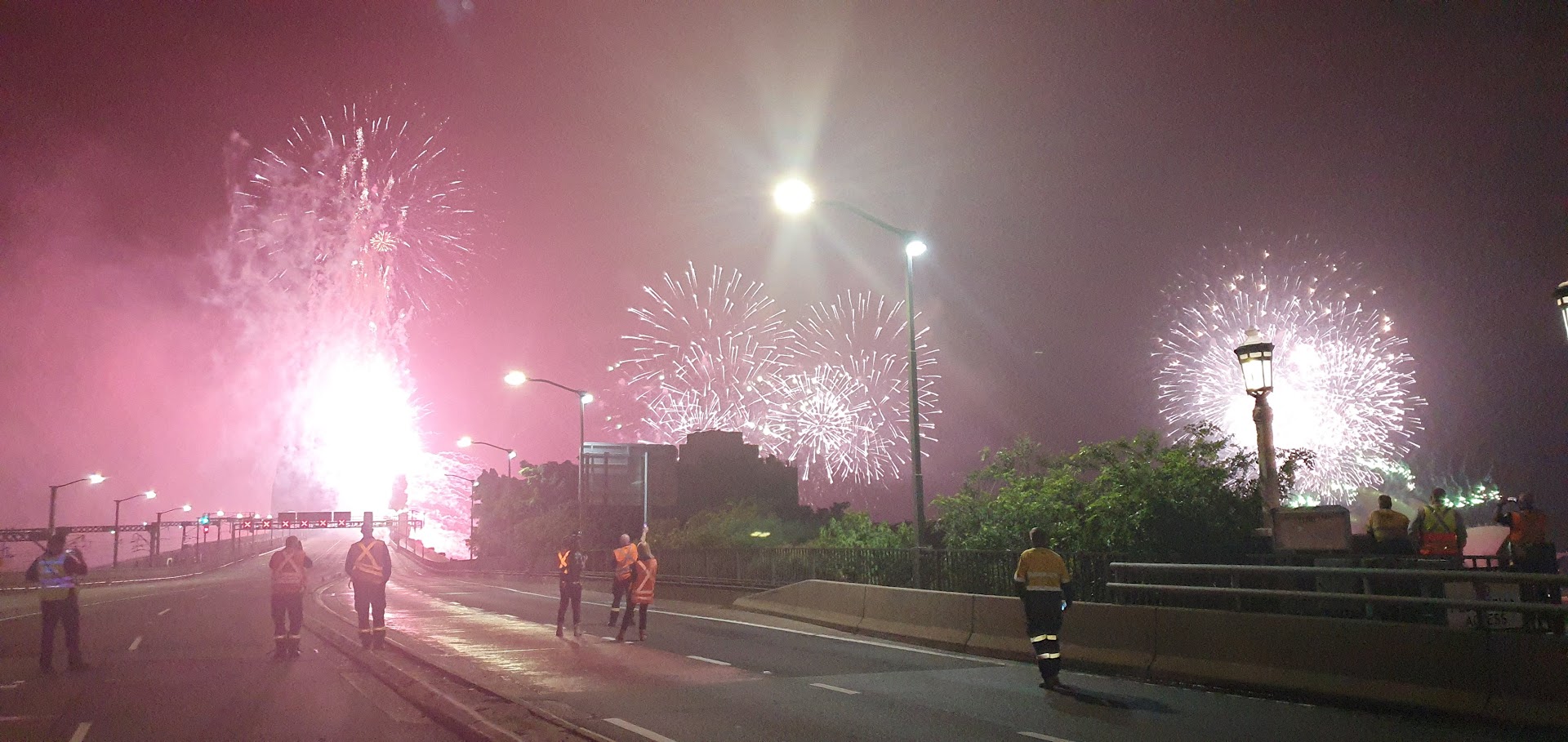 Spectacular fireworks display with a group of workers on a bridge, creating a vibrant and celebratory atmosphere under the night sky.