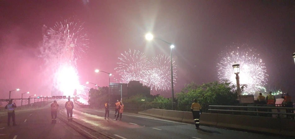 Spectacular fireworks display with a group of workers on a bridge, creating a vibrant and celebratory atmosphere under the night sky.