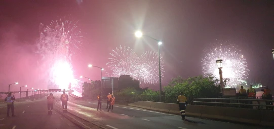 Group of workers in high-visibility vests watching large fireworks display over a bridge at night