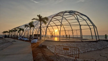 Large geodesic frame structure on a coastal site at sunset with palm trees