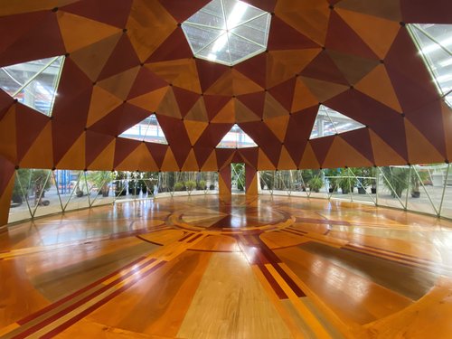 Interior view of a dome structure featuring a geometric ceiling pattern with triangular windows, and a polished wooden floor with inlaid design.