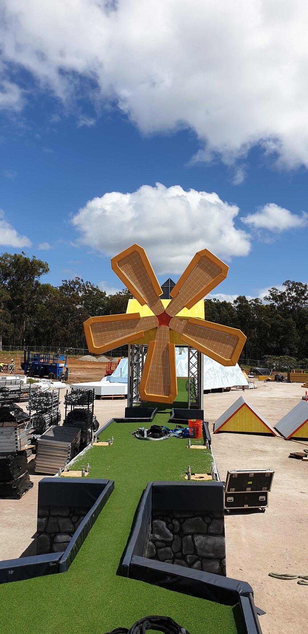 Outdoor shot showcases a miniature golf windmill on an artificial turf course under a blue sky with scattered clouds, suggesting fun and leisure.