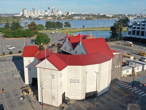 Aerial view of the Shakespeare Globe Theatre replica in Perth, Australia, with a red roof, set against the city skyline and Swan River.