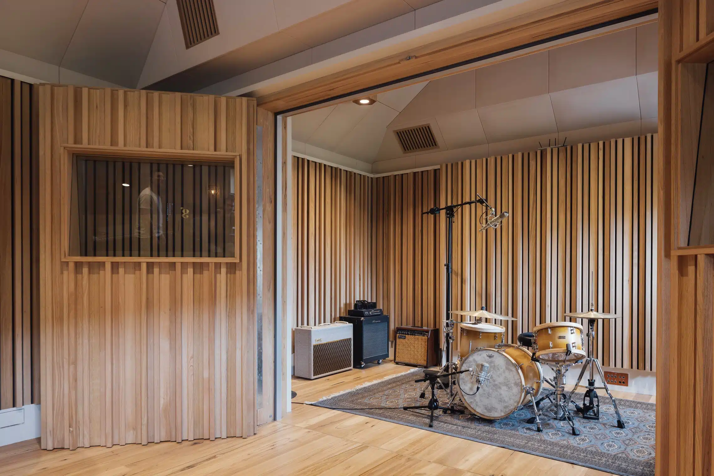 Interior of a music studio featuring a drum set, microphone, and soundproofing panels on the walls and ceiling, creating an intimate space.