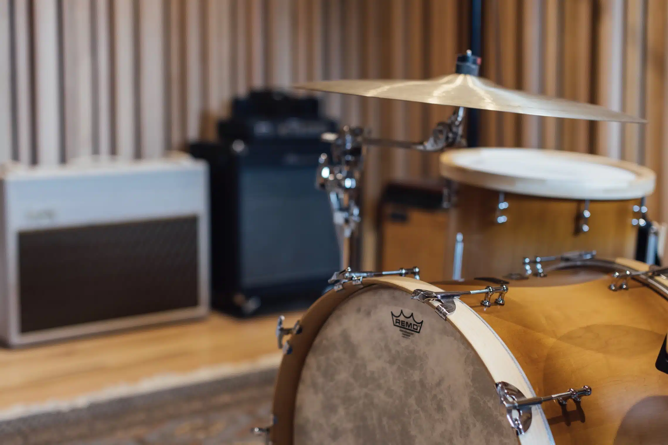 Close-up shot of a vintage drum set including a bass drum, tom-tom, and cymbal, with studio amplifier in a music recording space.