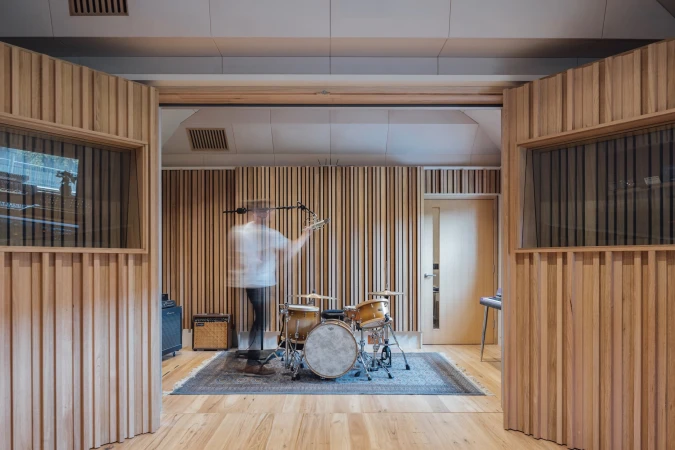 Motion blurred person setting up drum kit inside recording studio with wood panel walls in Melbourne by Ginger Studios.