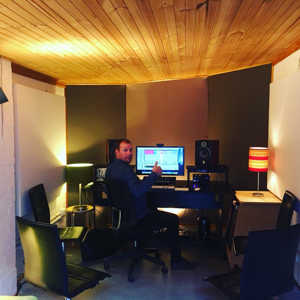 Man in music studio giving thumbs up while sitting in front of computer with audio editing software and studio monitors.
