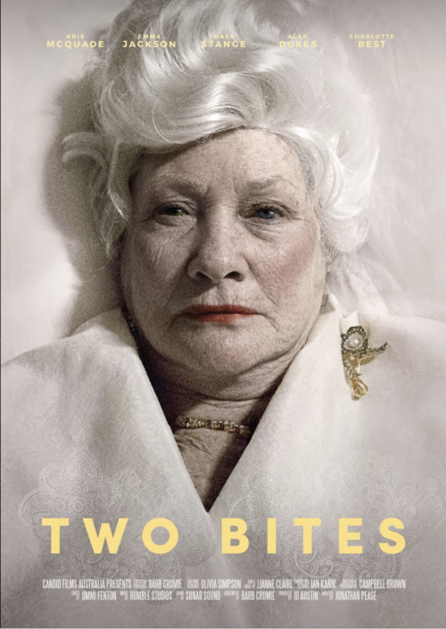 Close-up portrait of an elderly Caucasian woman with white hair wearing a formal white jacket, and a gold brooch, against a neutral background.