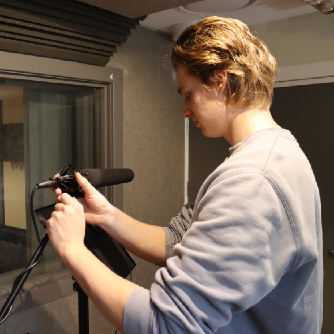 Man adjusting microphone in sound booth. Close-up view of adult male wearing grey sweater in professional recording environment.