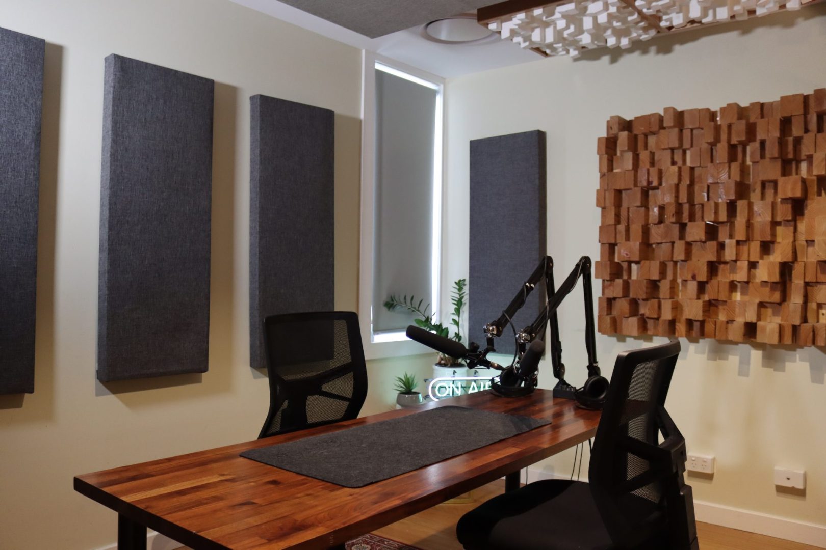 Podcast recording studio featuring a wooden table with microphones, acoustic panels, and soundproofing elements in a neutral-toned interior.