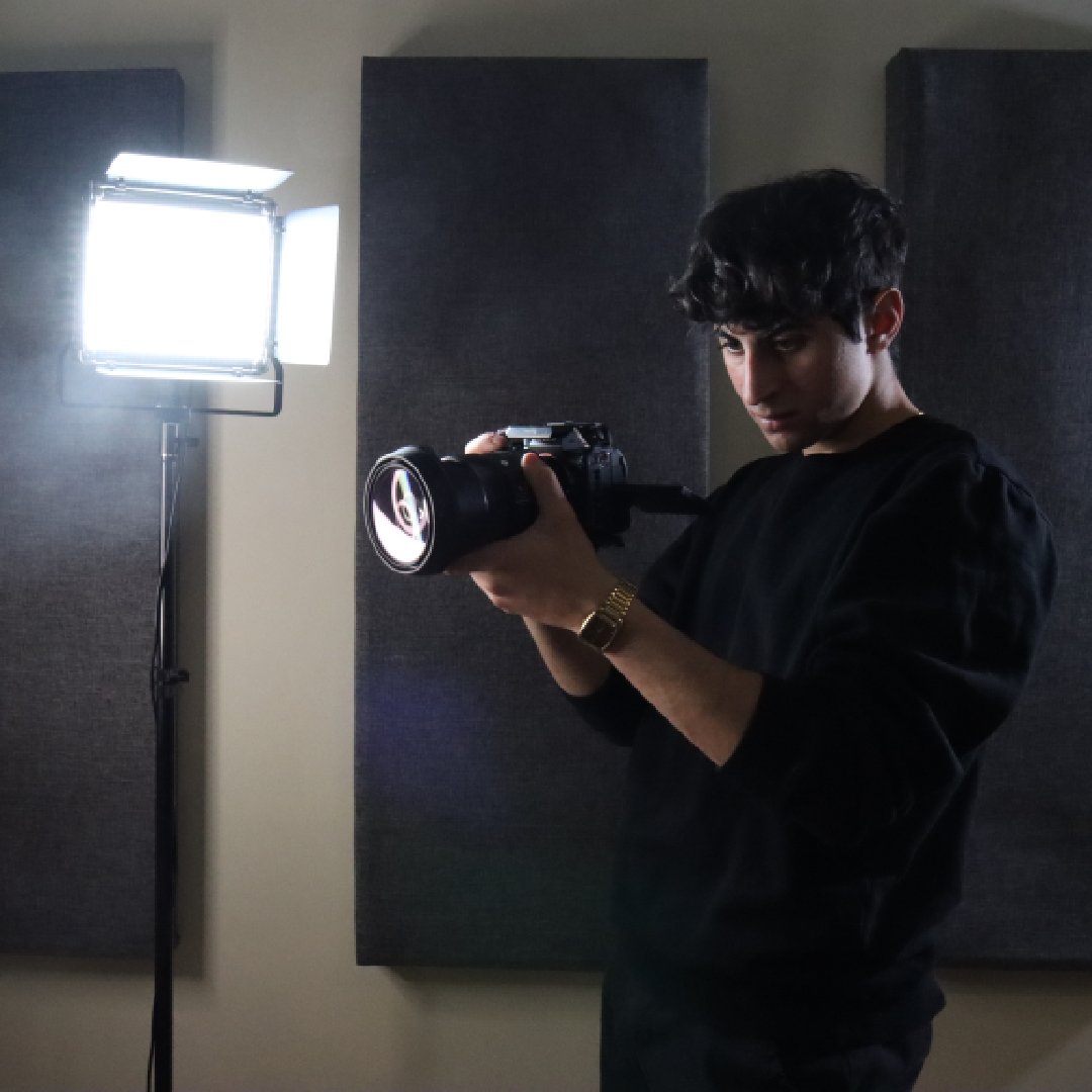Adult male with DSLR camera, studio lighting, taking a picture. The subject is centered in the frame against a dark grey background.