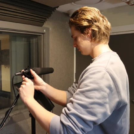 Man adjusting a studio microphone on a stand inside a recording booth by King Sound Studios