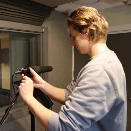 Man adjusting a studio microphone on a stand inside a recording booth by King Sound Studios