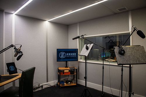 A sound recording studio is shown with microphones, headphones, computers, and acoustic paneling for audio recording and broadcast.
