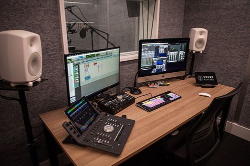 Professional recording studio with computer monitors, speakers, mixing console, and audio equipment on a wooden desk with grey walls.