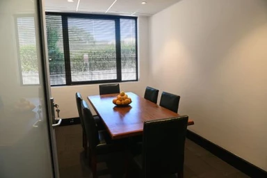 A wooden conference table surrounded by black chairs in a modern office interior with a window showing outdoor greenery.