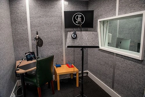 Sound Kitchen recording booth interior featuring acoustic wall panels, microphone on stand, and wooden desk.