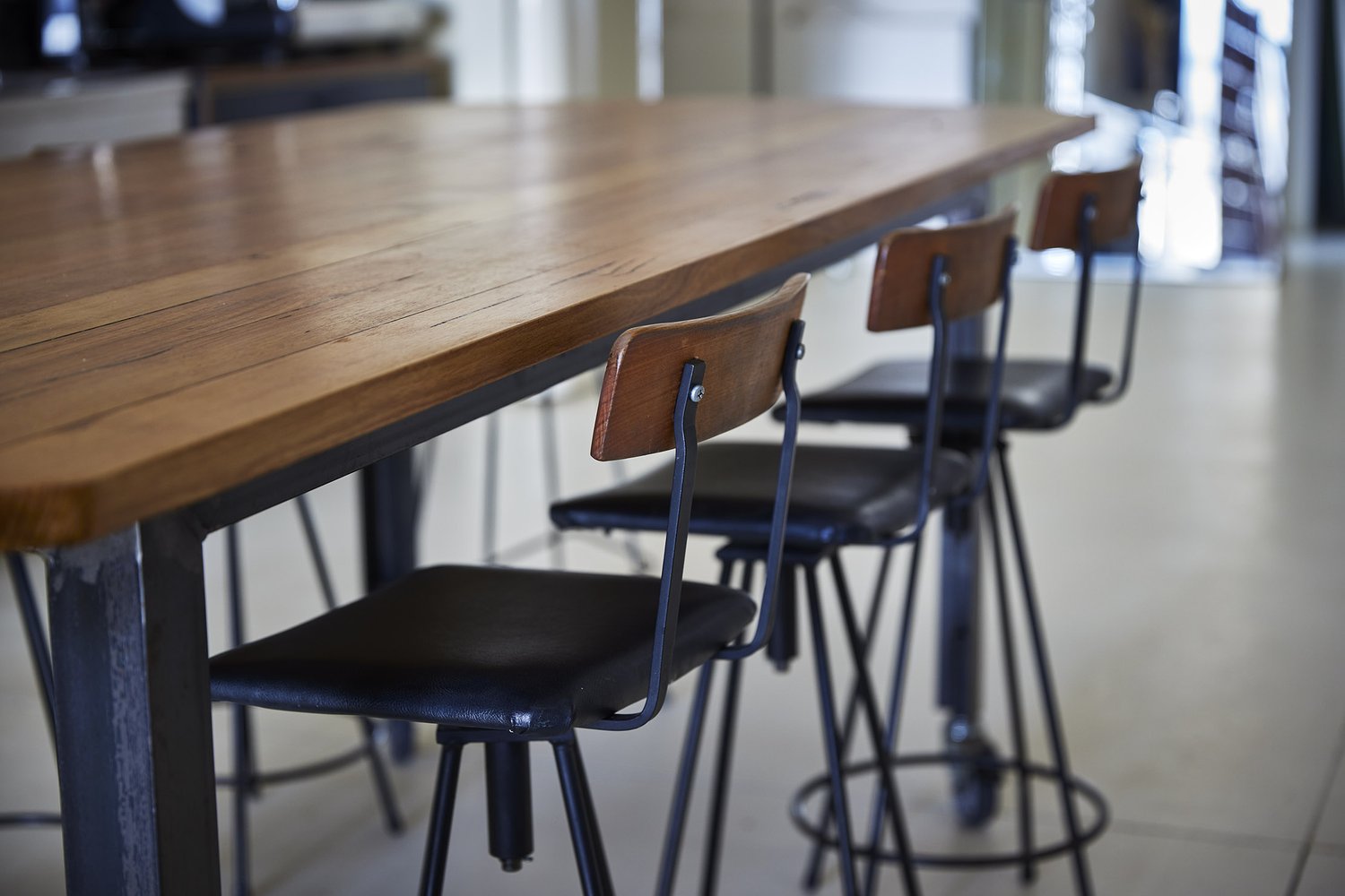 Wooden countertop and black metal bar stools with wooden backs in an indoor setting, creating a minimalist, functional aesthetic.