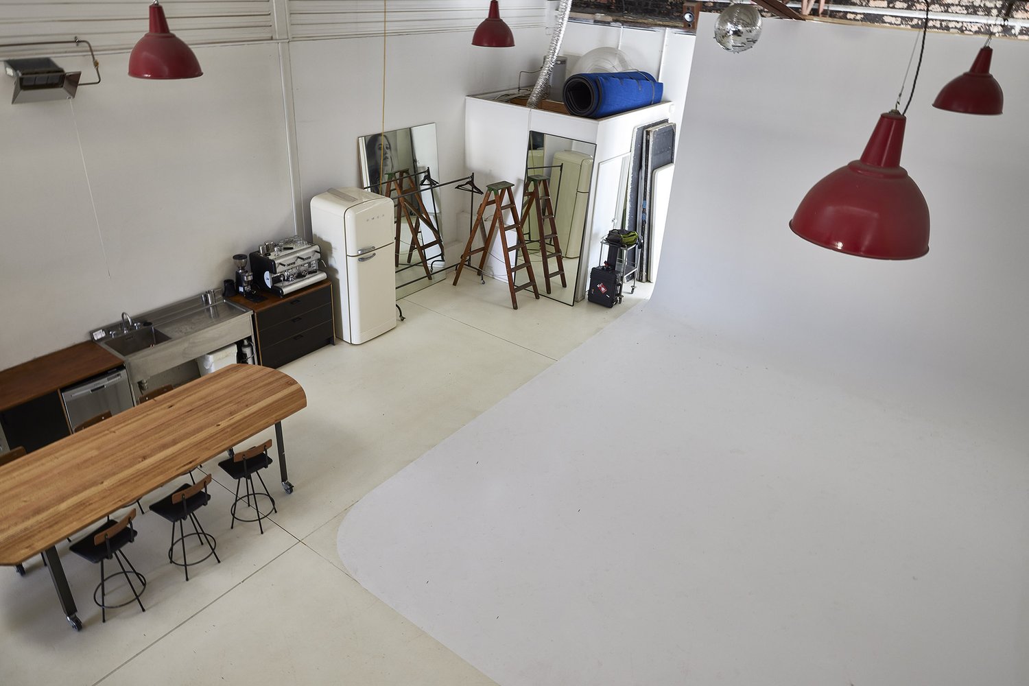 Spacious photo studio with a white backdrop, kitchen area, and red pendant lights, creating a bright and versatile shooting environment.
