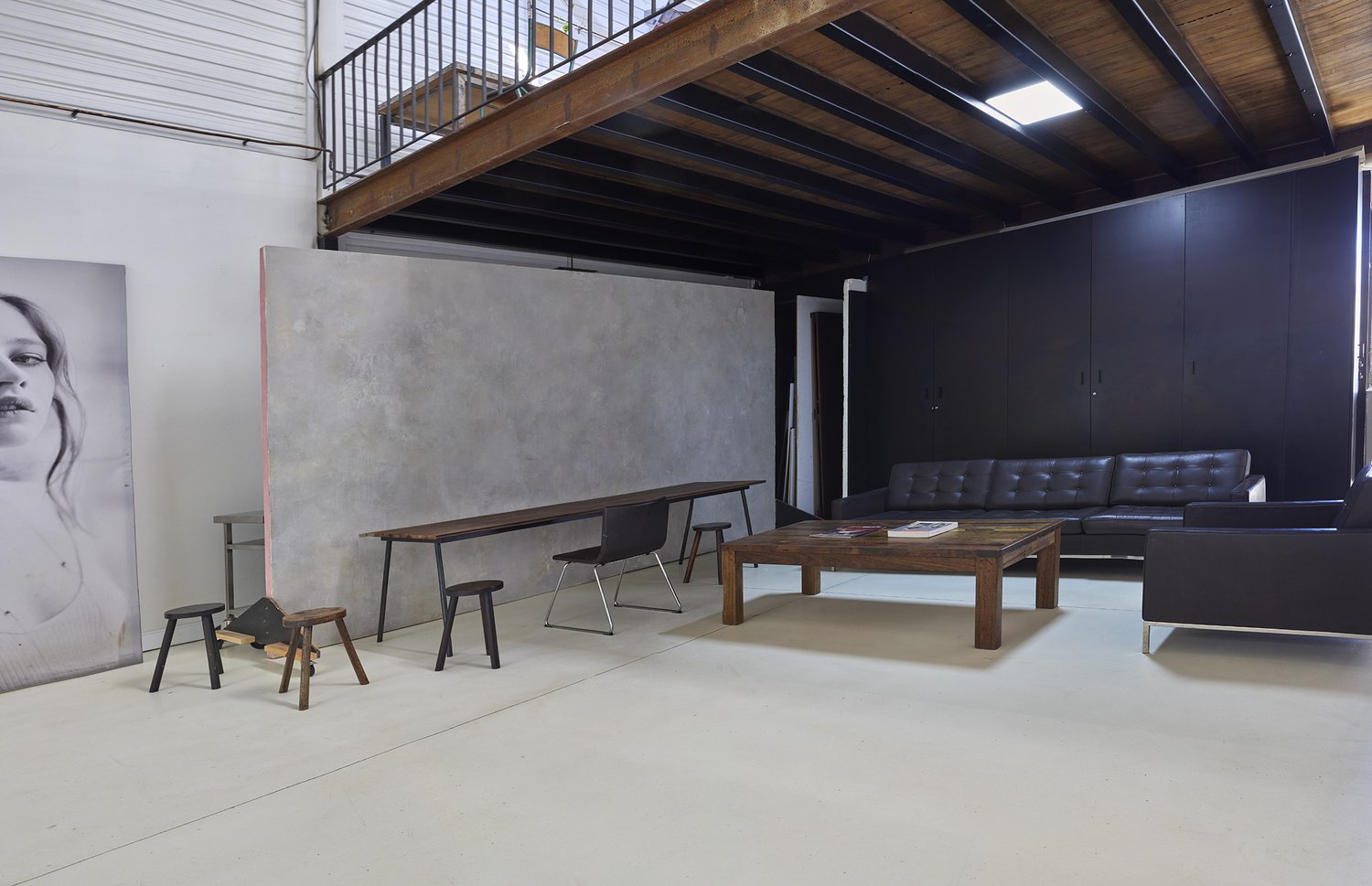 Interior photo of a photo studio with a long wooden table, black leather couch, art pieces and stools in a bright, spacious setting.