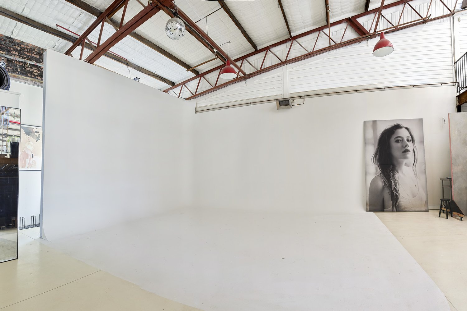 Brightly lit photography studio with white walls, reflective floor, disco ball, hanging red lamps, and black and white portrait on a wall.