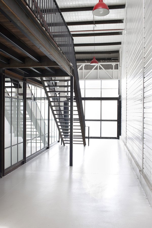 Architectural shot of a modern office interior featuring a metal staircase, white floors and walls, and industrial red pendant lights.