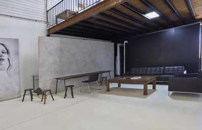Spacious photo studio interior with a polished concrete floor, mezzanine level, dark sofa, wooden coffee table, and textured partition wall