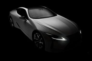 High-angle studio shot of a white sports car against a deep black background with illuminated headlights