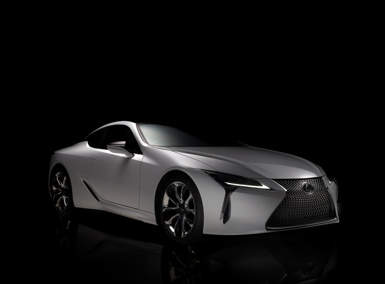 Sleek silver Lexus LC coupe showcased in a studio setting, bathed in dramatic lighting against a stark black background.