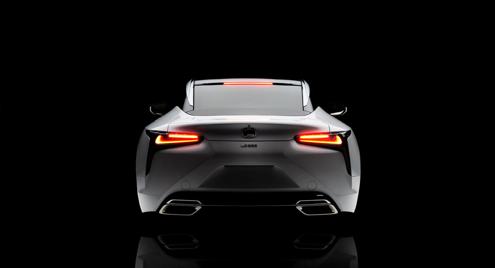 Rear view of a silver Lexus LC 500 sports car against a dark background showcasing its taillights, exhaust pipes, and sleek design.