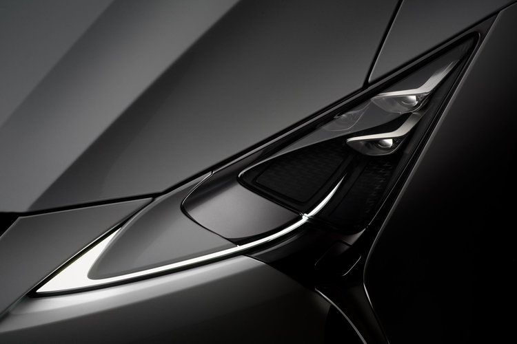 Close-up studio shot of the front headlight and sleek, dark grey body panels of a modern luxury car, capturing its refined design.